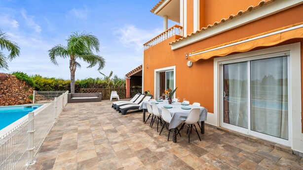 Ein Poolbereich mit einer Terrassentischgruppe, einem Pool und einem Gebäude mit Balkon.