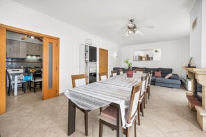 Un espace repas avec une longue table, des chaises et une cuisine en arrière-plan.