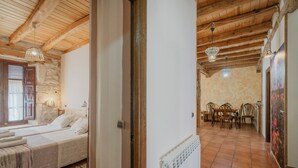 Une pièce comprenant un lit, un plafond en bois, un mur en pierre, un coin repas avec des chaises et un radiateur.
