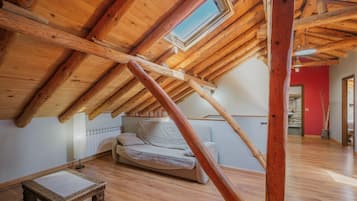 A loft bedroom with a sloped ceiling, wooden beams, a skylight, a sofa, and a small table.