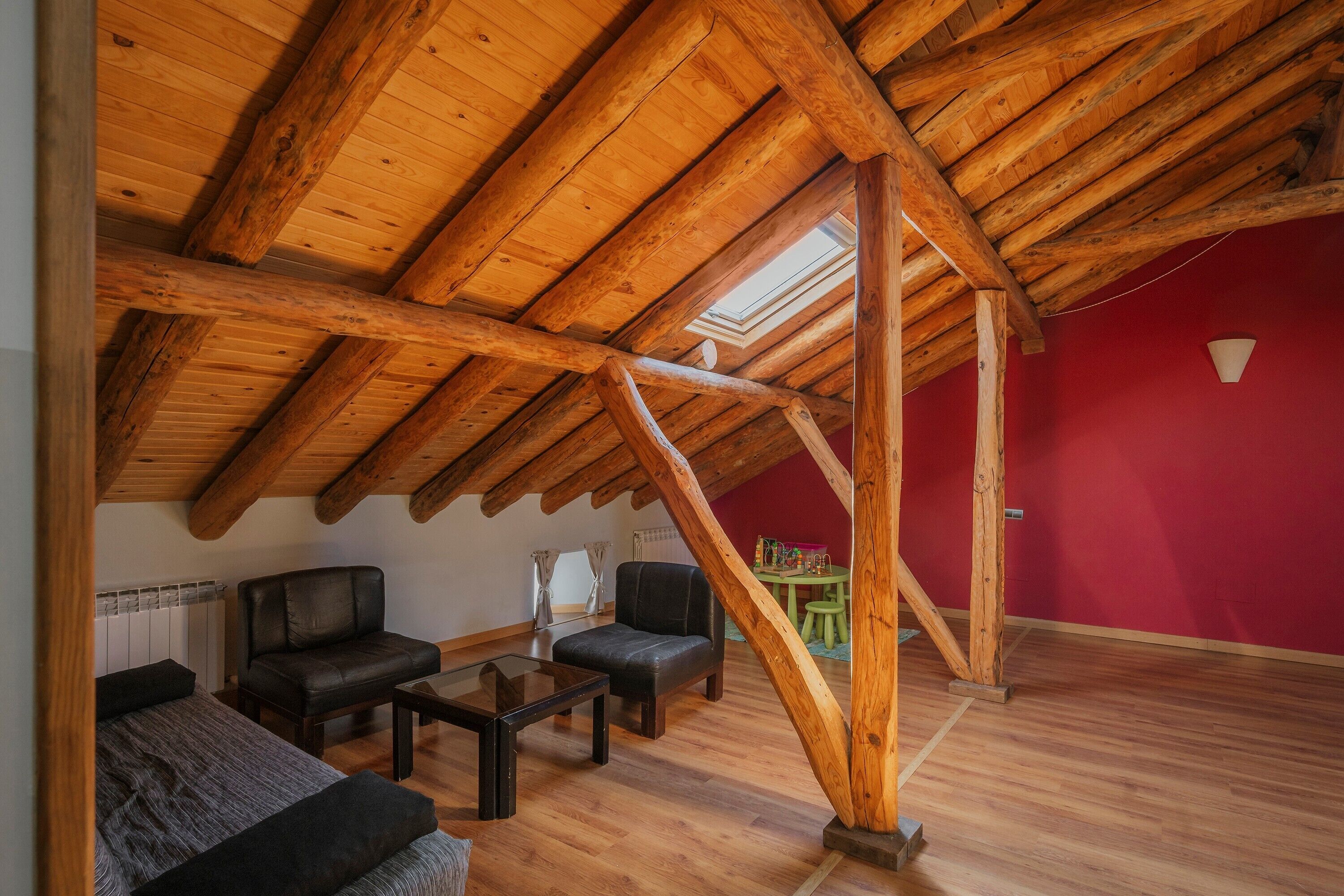 Una habitación en el ático con vigas de madera, una pared roja y un tragaluz.