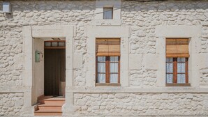 Un bâtiment en pierre avec une porte, deux fenêtres avec volets et une antenne parabolique sur le toit.