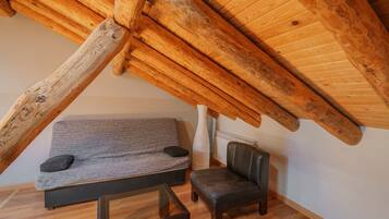 Una habitación estilo loft con vigas de madera a la vista, un sofá gris, un sillón de cuero y una mesa de centro de vidrio.