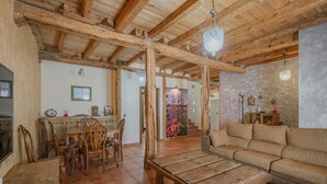 Un intérieur rustique avec des poutres en bois, un coin repas avec des chaises, un canapé et un sol carrelé.