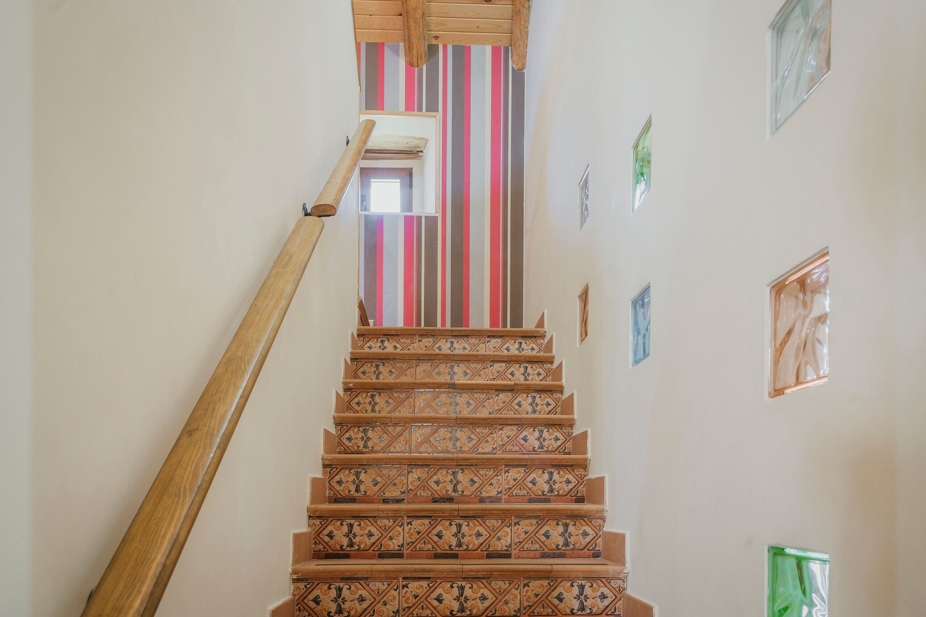 Een trap met sierlijke patronen, een houten leuning en een gestreept muur op de achtergrond.