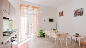 Una cocina moderna con un lavamanos, estufa y armarios, un comedor con mesa y sillas, y una sala de estar con sofá y obras de arte en las paredes.