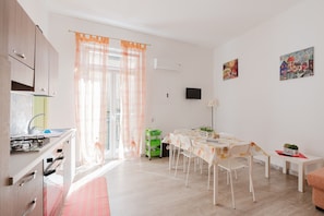 Une cuisine moderne équipée d’un évier, d’une cuisinière et de placards, un coin repas avec une table et des chaises, et un espace de vie agrémenté d’un canapé et d’œuvres d’art aux murs.