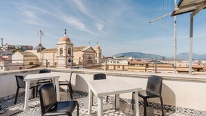 Una terraza en la azotea con mesa y sillas, suelo estampado y vistas a una iglesia y montañas.
