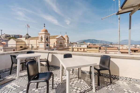 Une terrasse sur le toit, avec une table et des chaises, un sol à motifs et une vue sur une église et des montagnes.