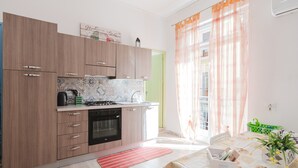 Cocina moderna con armarios de madera, estufa a gas y un lavamanos. Hay una zona de comedor con mesa y sillas, y una ventana con cortinas.