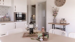 A kitchen with white cabinets, a microwave, a clock, and a table with wine glasses, a bottle, and jars. - Vacation Home 'Los Barranquillos' with Sea View, Private Pool, and Wi-Fi (Las Palmas)