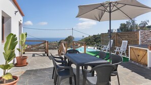 A patio with a table, chairs, an umbrella, potted plants, and a view of the sea. - Vacation Home 'Los Barranquillos' with Sea View, Private Pool, and Wi-Fi (Las Palmas)