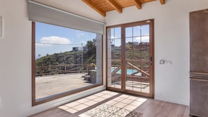 A room with a large sliding glass door leading to an outdoor area with a pool and a view of a hillside. - Vacation Home 'Los Barranquillos' with Sea View, Private Pool, and Wi-Fi (Las Palmas)