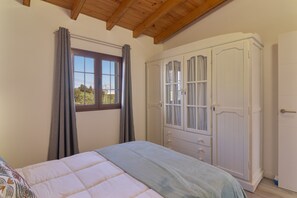 A bedroom with a bed, a wardrobe, a window with curtains, and a wooden ceiling. - Vacation Home 'Los Barranquillos' with Sea View, Private Pool, and Wi-Fi (Las Palmas)