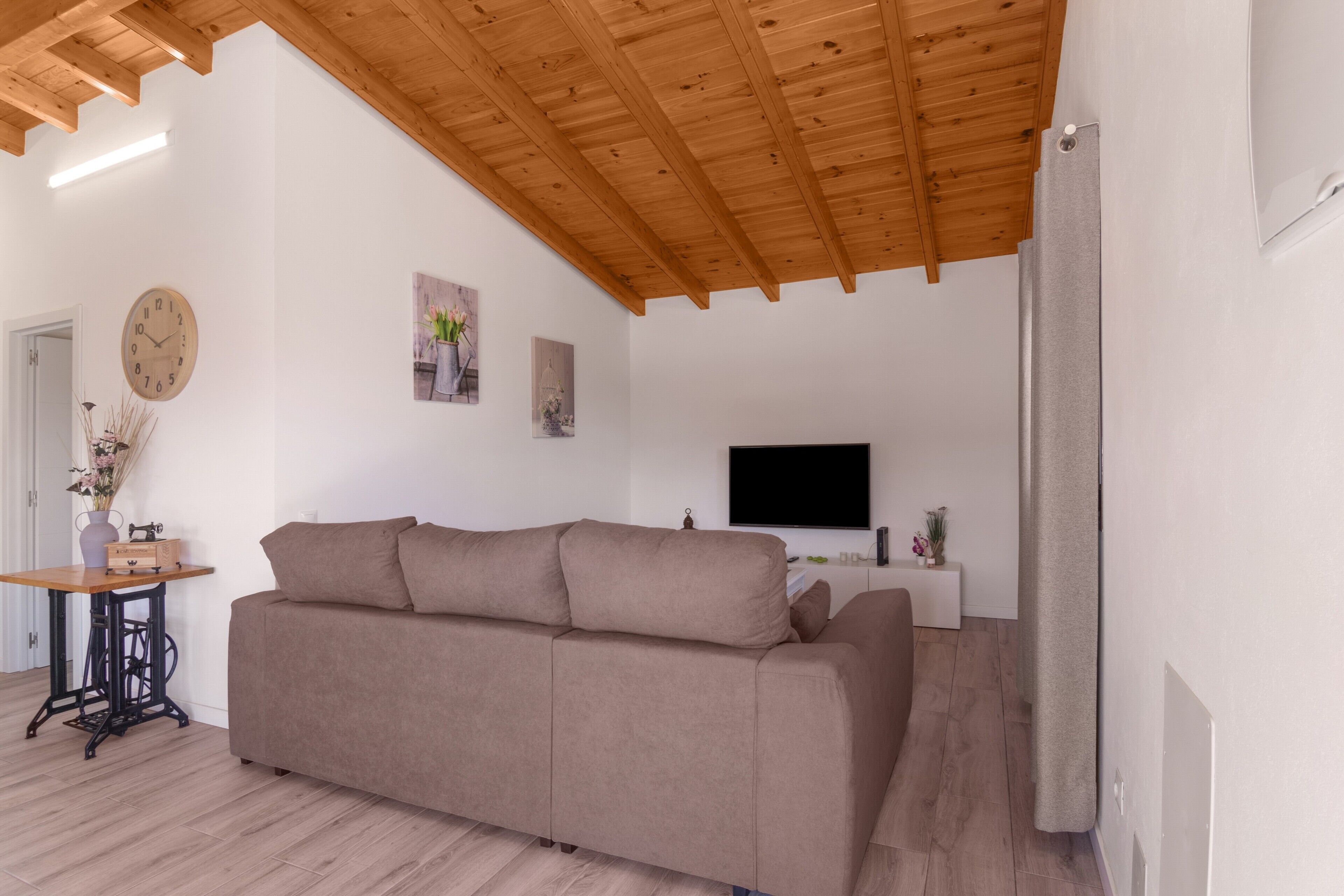 Een woonkamer met een bank, houten balken in het plafond, een klok en een flatscreen-televisie.