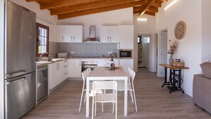 A modern kitchen with white cabinetry, stainless steel appliances, a wooden ceiling, and a dining area with white chairs. - Vacation Home 'Los Barranquillos' with Sea View, Private Pool, and Wi-Fi (Las Palmas)