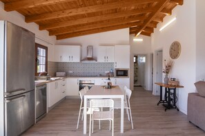 A modern kitchen with white cabinetry, stainless steel appliances, a wooden ceiling, and a dining area with white chairs.