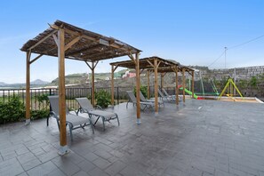 Ein überdachter Außenbereich mit Sitzgelegenheiten und einem Spielplatz im Hintergrund.