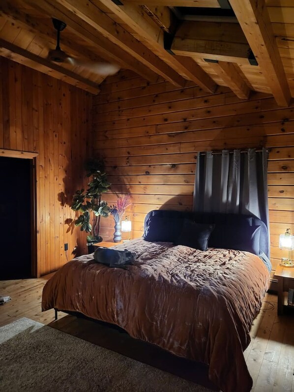 A wooden-paneled bedroom with a bed, a ceiling fan, and a nightstand with a lamp.