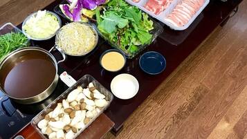 Een tafel met diverse etenswaren en toevoegingen, zoals plakjes vlees, groenten, champignons en een soepketel.