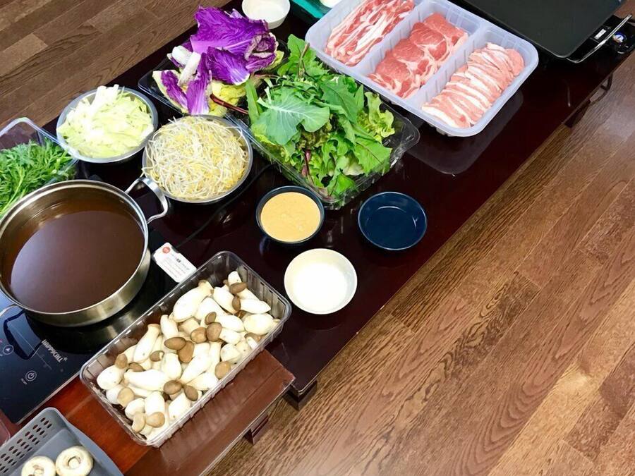 Een tafel met diverse etenswaren en toevoegingen, zoals plakjes vlees, groenten, champignons en een soepketel.