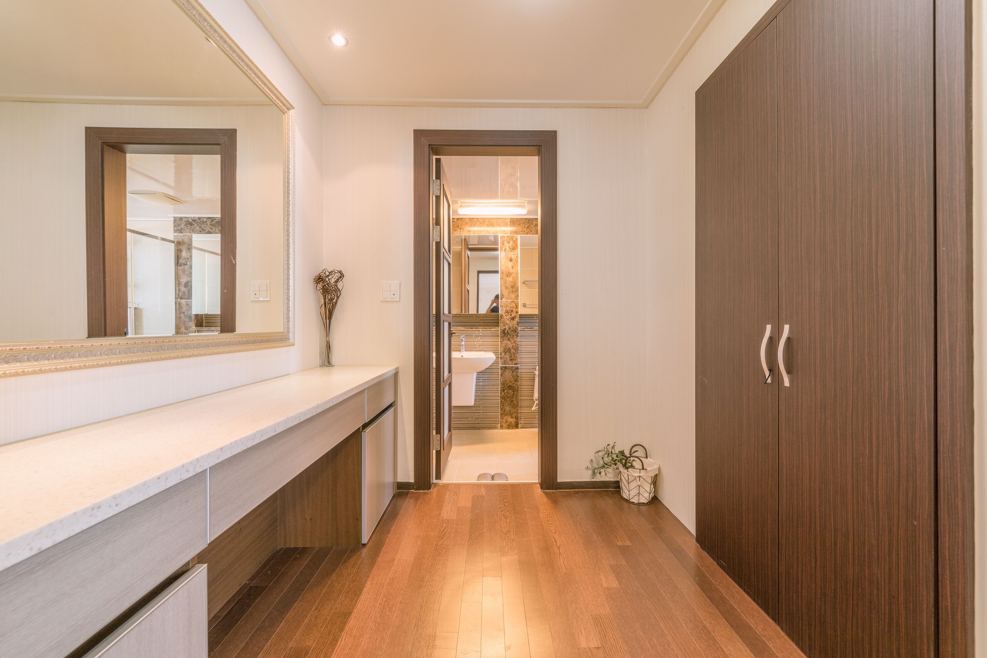 A hallway with a wooden floor, a mirror, a wooden cabinet, and a wardrobe.