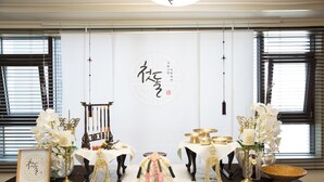A traditional East Asian styled room with a central table displaying calligraphy, surrounded by floral arrangements and traditional items. - Sejong Party House  (Busan)