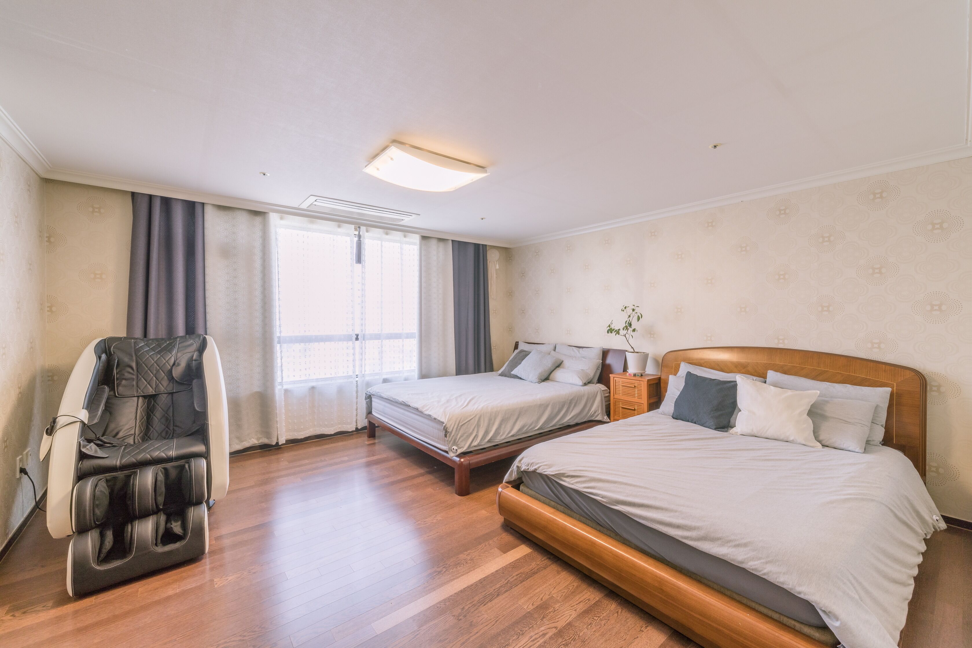 Quarto de hotel com duas camas, uma poltrona de massagem, mesa de cabeceira e janela com cortinas.