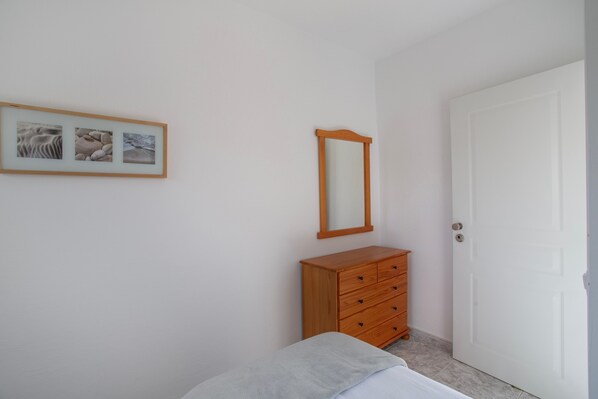 A bedroom with a bed, a wooden dresser, a mirror, and a framed picture on the wall.
