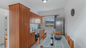 A kitchen with wooden cabinets, a dining table with chairs, a refrigerator, and a window with a view. - Los Adejo Vacation Home with Shared Heated Pool, Terrace, and Wi-Fi (Moya)