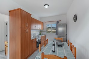 A kitchen with wooden cabinets, a dining table with chairs, a refrigerator, and a window with a view.