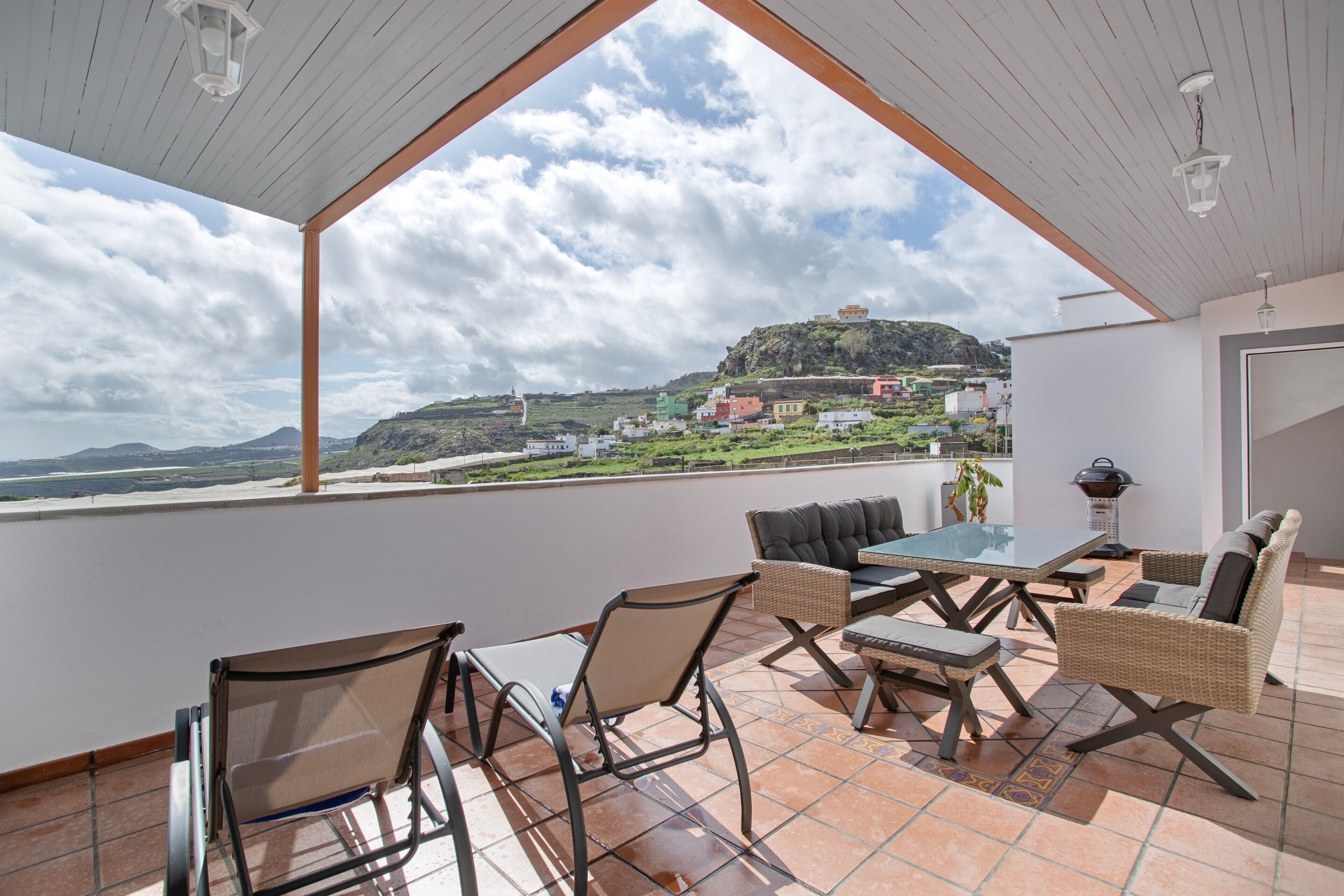 Eine Terrasse mit Tisch und Stühlen, Blick auf einen Hügel mit Gebäuden und einem klaren Himmel.