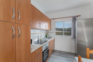 A kitchen with wooden cabinets, a stainless steel refrigerator, a window with a view, and a wooden chair. - Vacation 'Los Adejo' with Shared Terrace, Shared Garden and Wi-Fi (Moya)