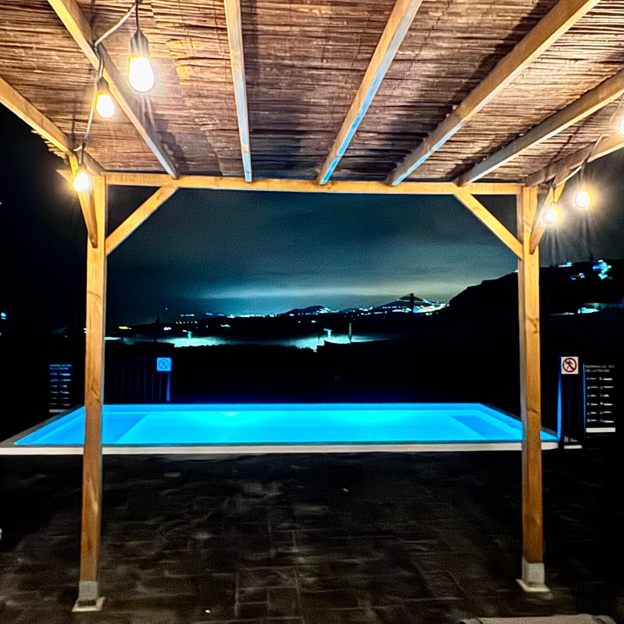 Una piscina al aire libre con una pérgola de madera sobre ella, rodeada de un paisaje oscuro.