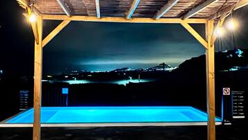 Una piscina al aire libre con una pérgola de madera sobre ella, rodeada de un paisaje oscuro.