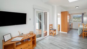 A modern interior with a wooden desk, a flat-screen TV, a sliding glass door leading to a balcony, and a kitchen area with wooden cabinets. - Los Adejo Vacation Home with Shared Heated Pool, Terrace, and Wi-Fi (Moya)
