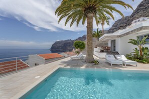 Una piscina con sillas de descanso, una palmera y vista al mar.