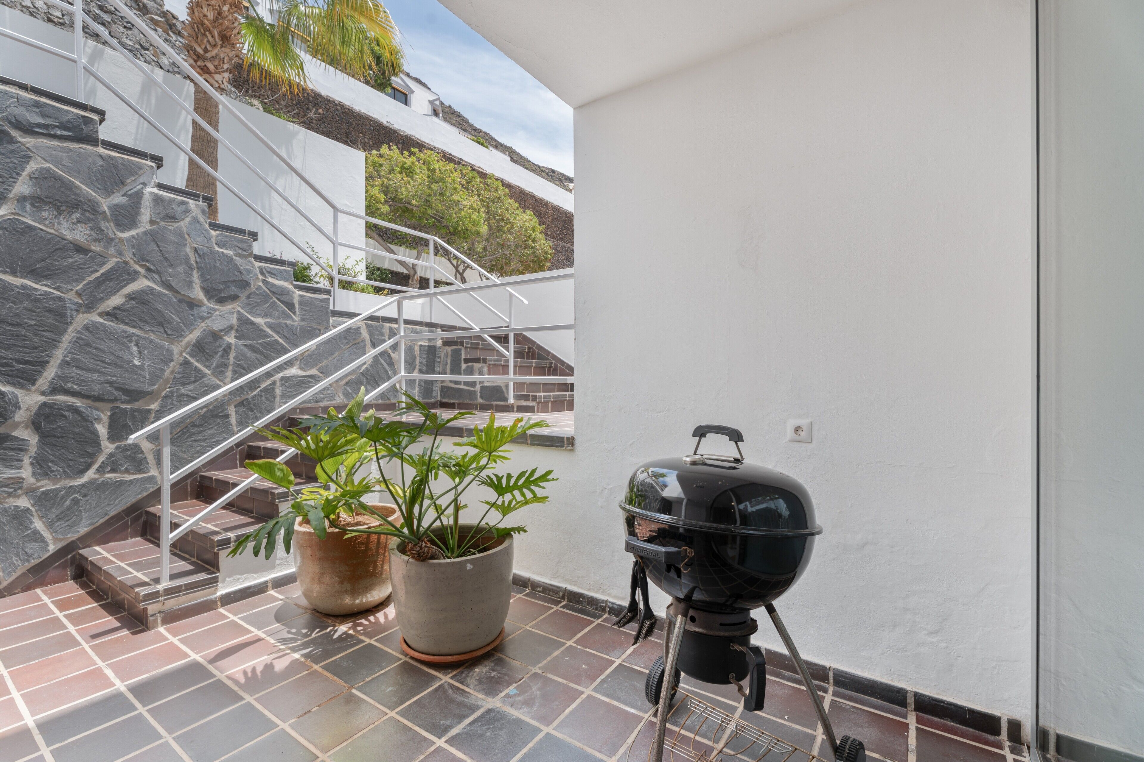 Eine Terrasse mit Steintreppe, einem Blumentopf und einem Grill.