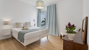 Un dormitorio con cama, mesita de noche, lámpara, cortinas y una planta en maceta.