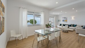 Una sala de estar moderna con una mesa de comedor de vidrio, sofás blancos y vista al mar.