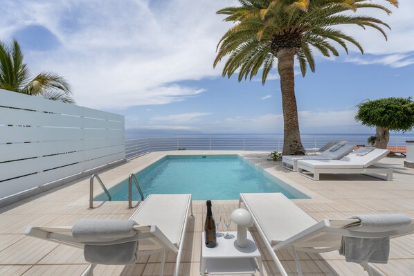 A pool area with lounge chairs, a bottle, and glasses, overlooking the sea.