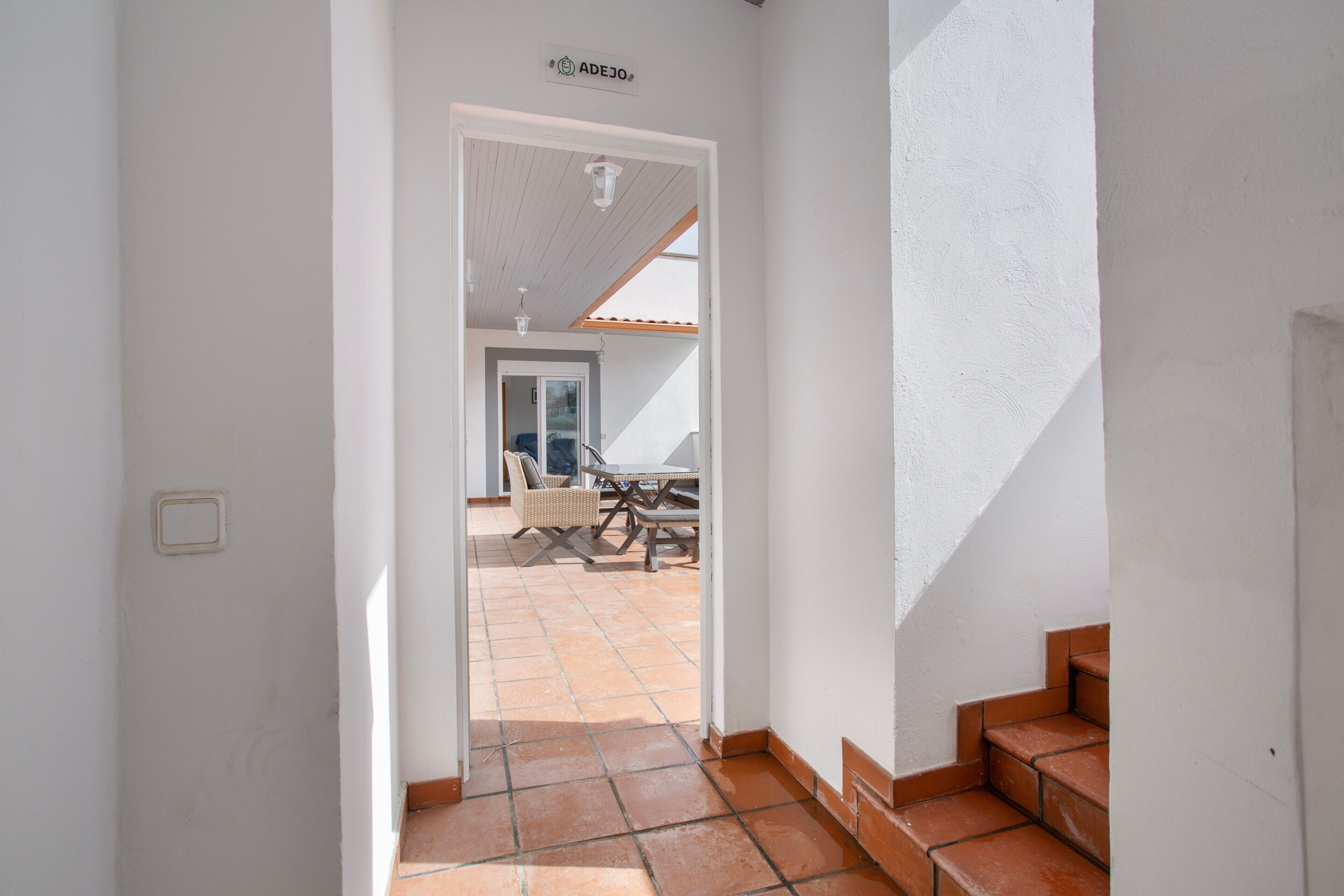 Un pasillo que conduce a un patio con una mesa y sillas, una escalera y un letrero sobre la puerta.