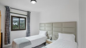Camera d'albergo con due letti, una finestra vista, un comodino con lampada e una luce a soffitto.