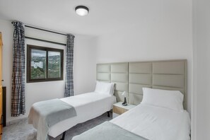 Habitación de hotel con dos camas, una ventana con vistas, una mesita de noche con lámpara e iluminación en el techo.