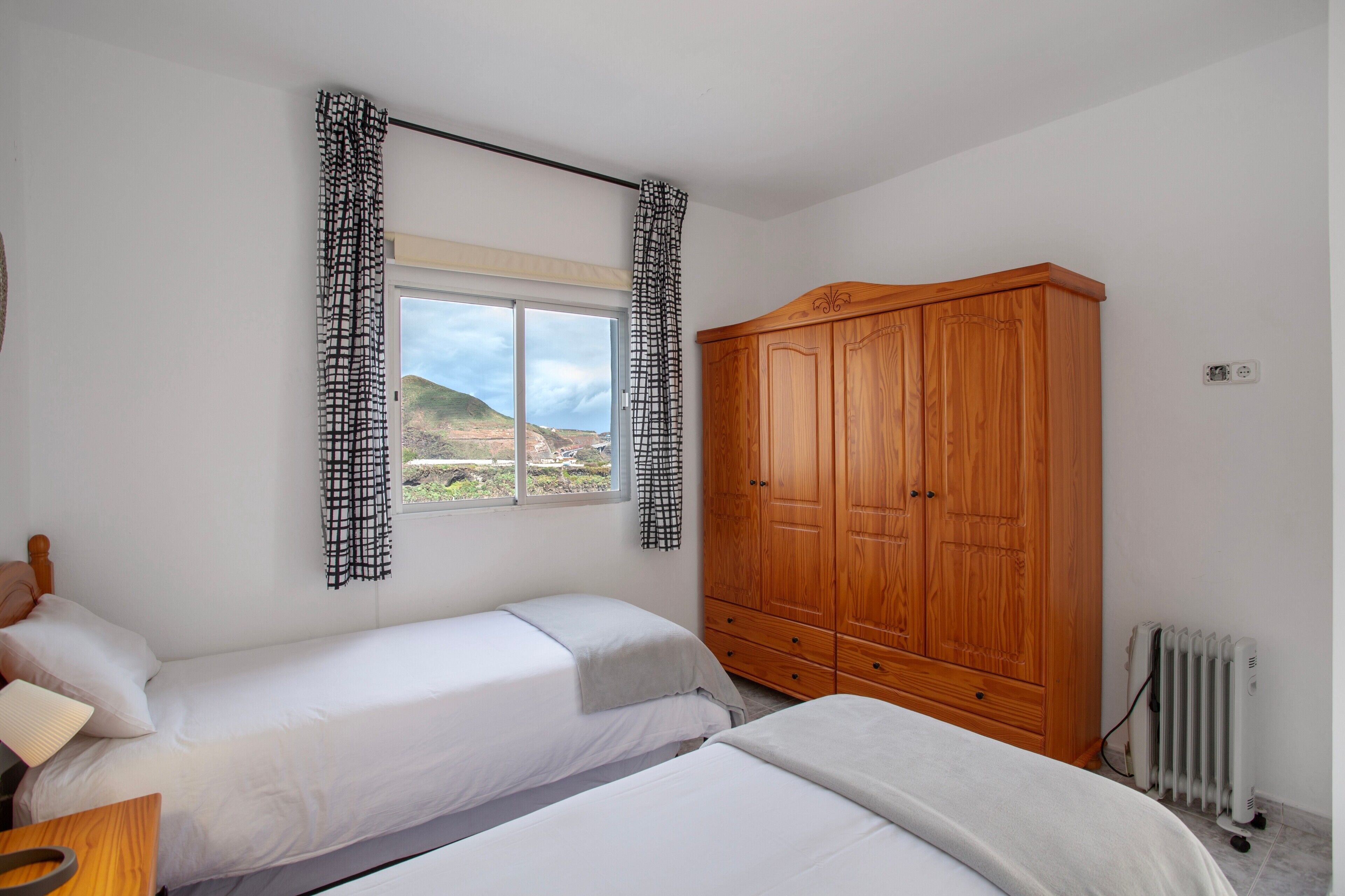 Une chambre avec deux lits, une armoire en bois, un radiateur et une fenêtre donnant sur un beau paysage.