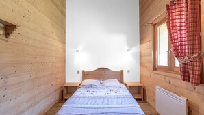 A single bed in a room with wooden walls, a window with red curtains, and a white radiator. - Chalet 'Les Laouchets -  8 Pers' with Mountain View, Balcony and Wi-Fi (Sixt-Fer-à-Cheval)