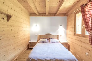 Une chambre dans une cabane en bois, avec un lit, deux tables de chevet et une fenêtre avec des rideaux.