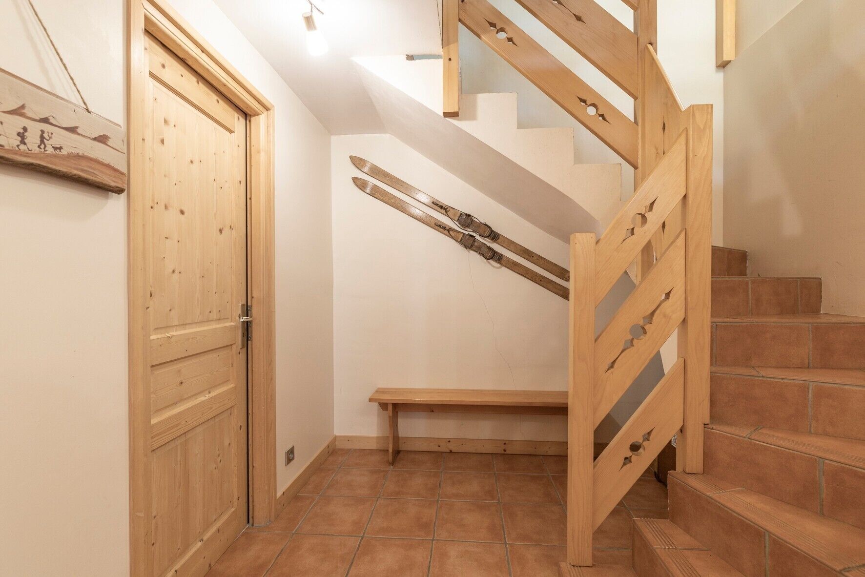 A wooden staircase with a bench, a wooden door, and a wall-mounted ski rack.
