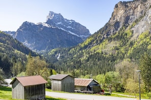 A mountain landscape with two rustic wooden buildings, a road, and a clear sky.