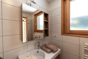A bathroom with a white sink, a mirror, a window, and a towel rack.